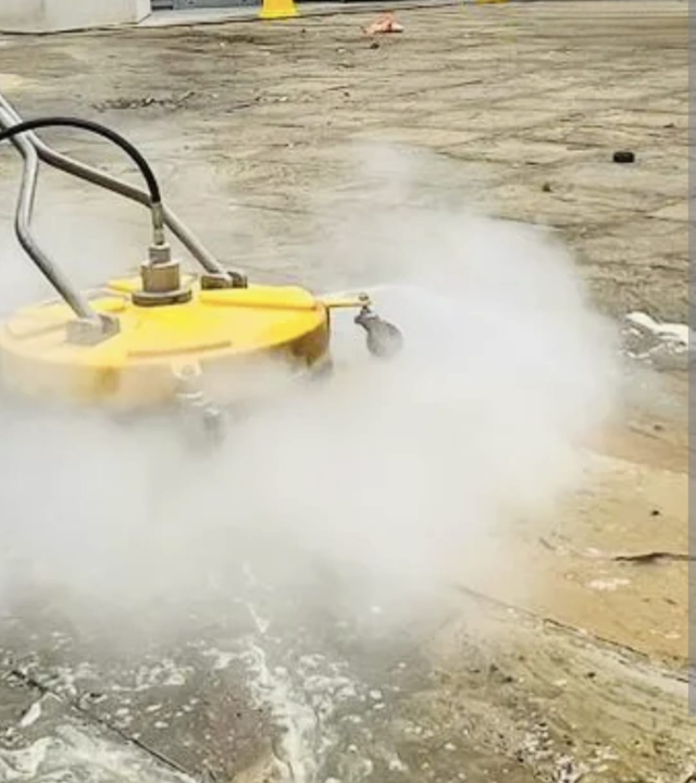 Steam cleaning a hard surface with a yellow surface cleaner attachment on a paved ground
